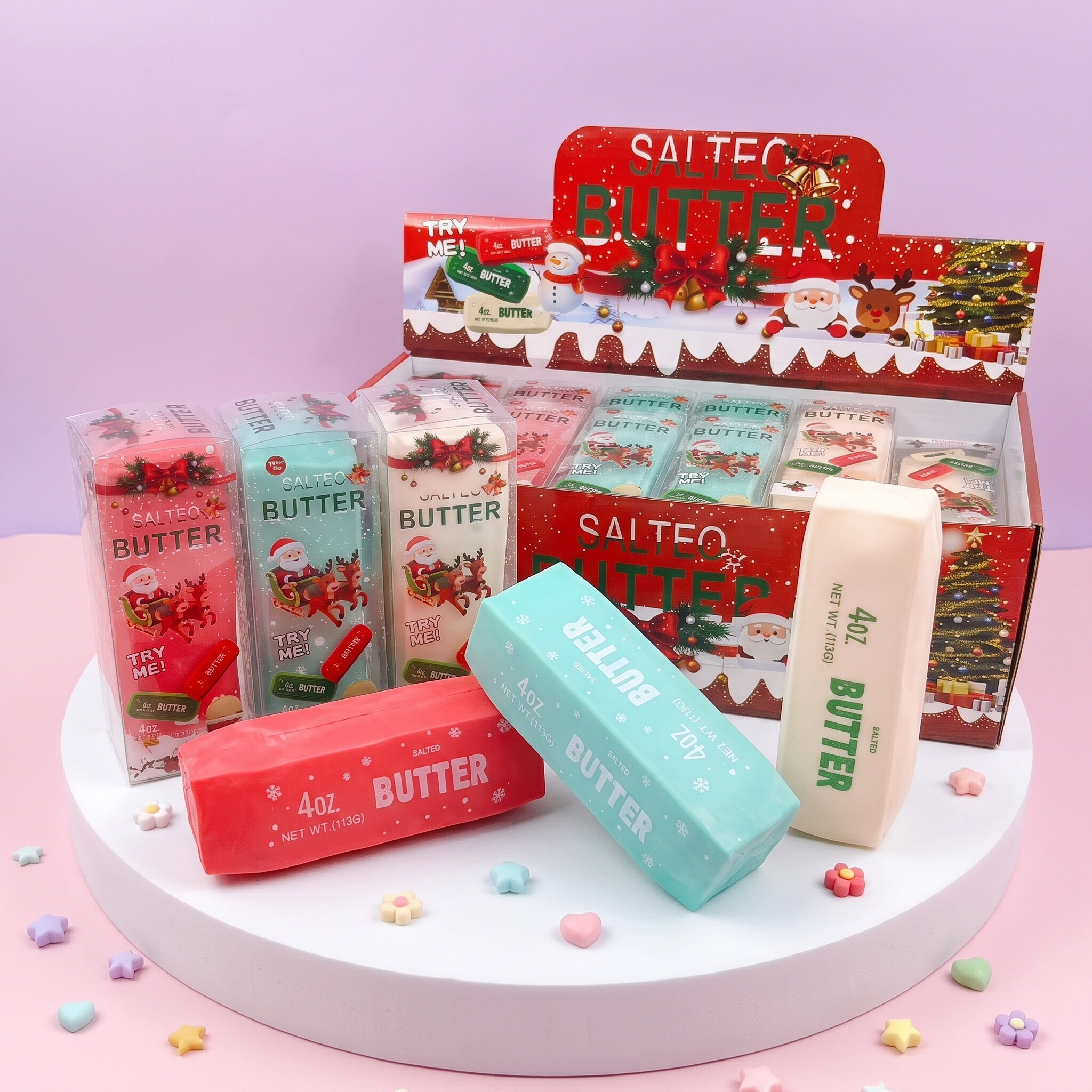 Squishy Beurre Craquant Noël 13 cm – Sensation TikTok Les 3 squishy beurre craquant Noël 13 cm rouge, vert menthe et blanc crème devant leurs boîtes illustrées Père Noël, renne et sapin, et le présentoir Salted Butter